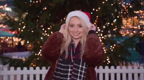 Young Woman Wearing Santa Hat by Christmas Tree