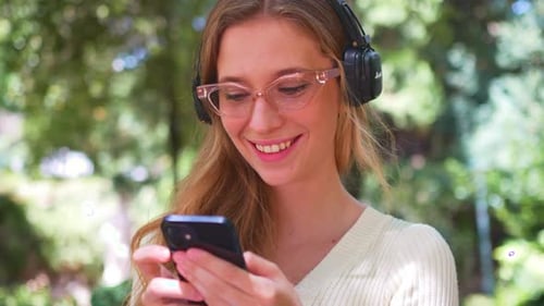 Young Woman with Headphones and Smartphone in Park