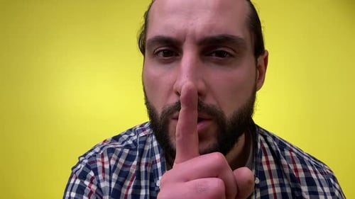 Man Saying Hush Shhh Gesture Close to Camera Isolated on Yellow