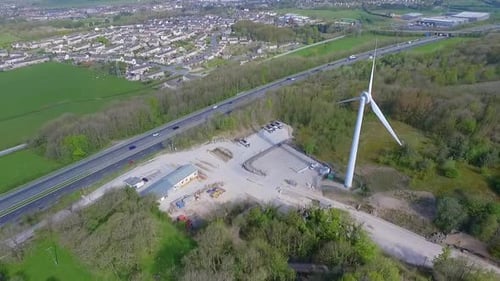 Aerial drone shot of single wind farm turbine next to a busy motorway freeway in Summer