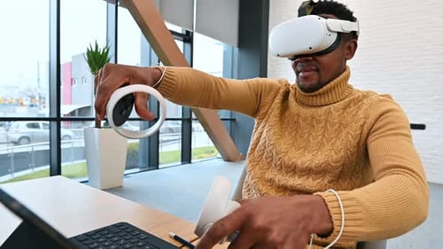 A black man exploring virtual reality using VR glasses and controllers in an office. Slow motion