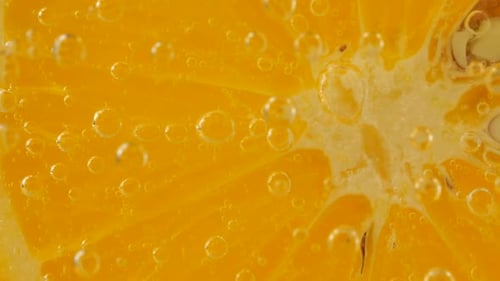 Eine Scheibe reifer Orange im Wasser sprudelt auf einem orangefarbenen Hintergrund.