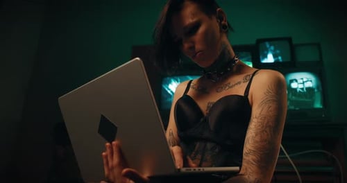 Woman Typing on Laptop with Monitors in Dark Room