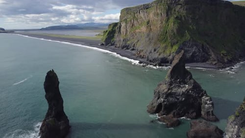 Waves crash onto the famous Black sand beach in Reynisfjara, Iceland. Drone slowly flies through tow