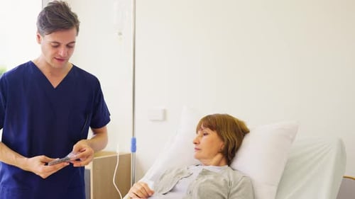 Young doctor or nurse man stand beside patient bed and explain about medicine for senior patient