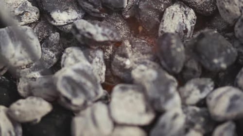 Charcoal being stirred in a black kettle grill during a summer picnic cook out.