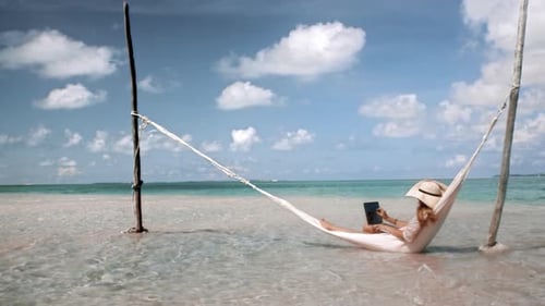 Of Woman Working on Laptop Computer on Hammock in Blue Ocean