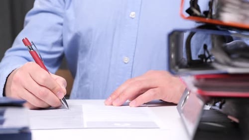 Office Worker Signing a Document with Stacked Files in the Foreground