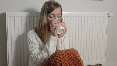 Worried Woman Sit Near Heating Radiator Under Blanket with Cup of Tea