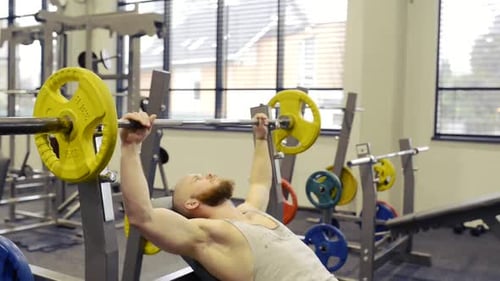 Young Muscular Man in Gym Lifting a Barbell on Bench