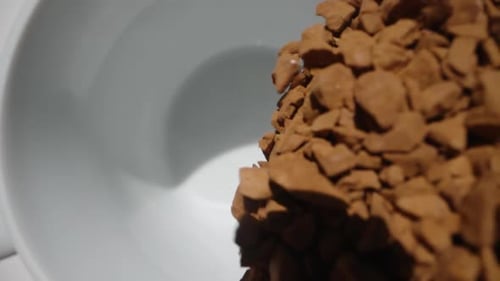 I pour instant coffee from a spoon into a white mug, slow motion. Dolly slider extreme close-up.