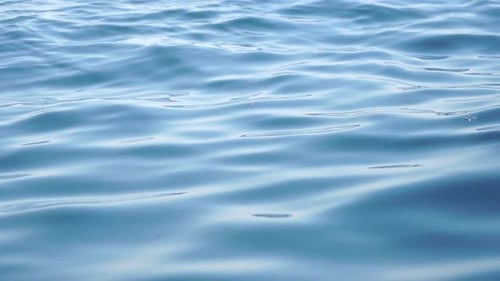 Sea Water Surface Camera Flies Over the Calm Azure Sea with Volcanic Rocky Shores on Background