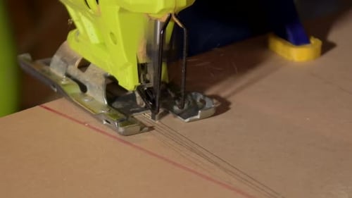 Close-up of electric jigsaw in action, men's hand cutting up wood board with a jigsaw
