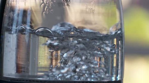Close up of water boiling in a clear glass pot. Beautiful bubbles cascade and rise to the surface t