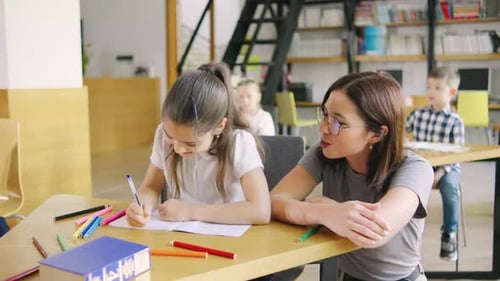 The Teacher is Sitting Next to a School Desk Providing Assistance and Recommendations to an