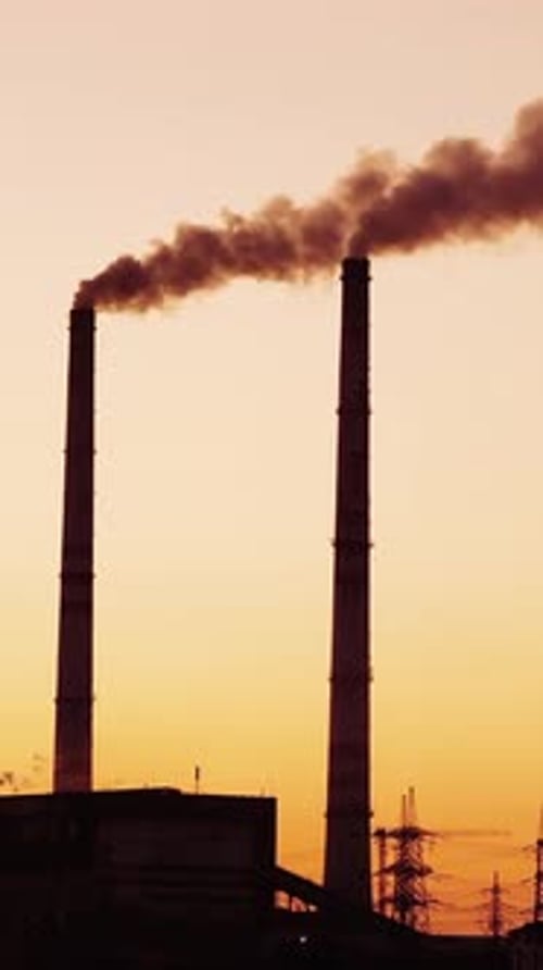 Smoke from industrial chimney. Silhouette of the power plant at sunset Vertical video