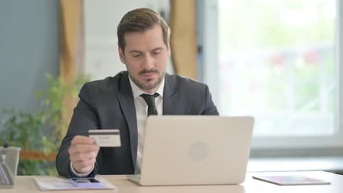 Man looks at credit card and laptop in office