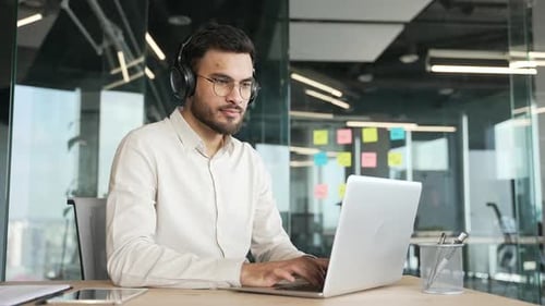 Focused businessman in wireless headphones works on a laptop sitting at a workplace in business