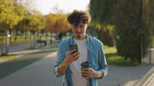 Front View of the Bearded Man Walking on the Street Using His Smartphone Texting With Friends