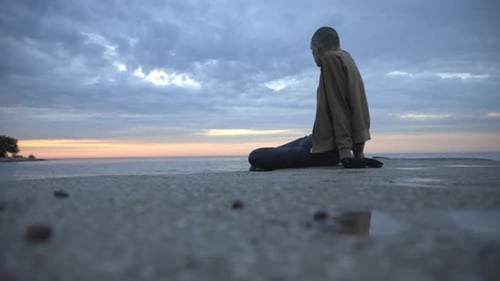 Low Angle View Of A Young Man Sitting On The Shore While Watching The Beautiful Nature - Wide Shot