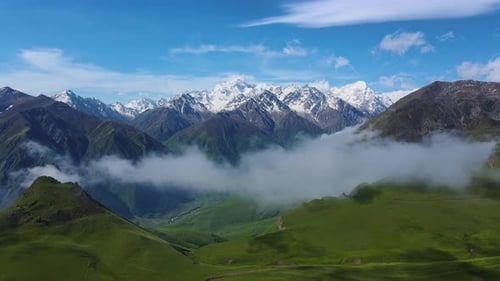 Enjoy the Scenic Mountain Range View with Green Hills and Snowcapped Peaks in a Serene Setting