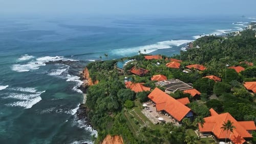 Vista aérea de un exclusivo complejo costero con villas de lujo, piscina infinita con vista al océano tropical