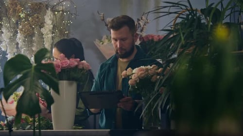 Male Florist with Digital Tablet Counts Flowers in Vase