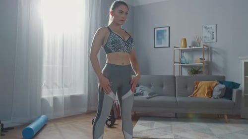 Strong and Fit Beautiful Busty Girl in an Athletic Top is Doing Squat Exercises in Her Bright and S