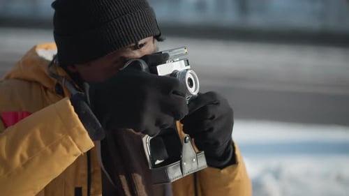 Photographer Adjusting Lens While Walking on Snowy Urban Path