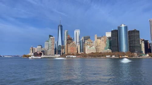 High skyline of New York city on a sunny day as a ferry sails across and a large bird flies around.