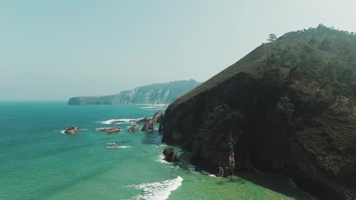Aerial view of dramatic coastal cliffs with turquoise waters, rocky outcrops, and a distant