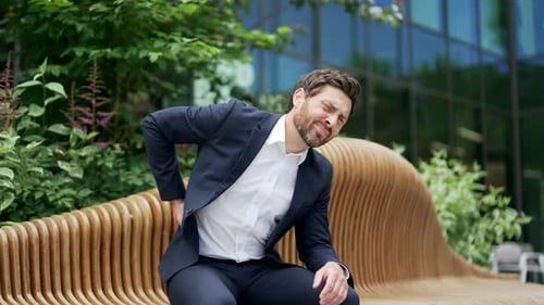 Man Sits on Bench with Lower Back Pain