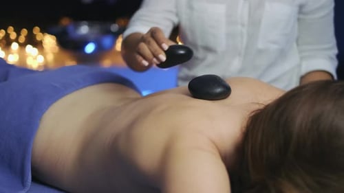 Im Massageraum legt die Masseuse der Frau heiße Steine auf den Rücken. Brennende Kerzenlichter i