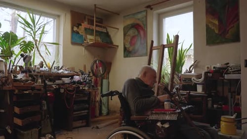 Senior Elderly Master Jeweler in Wheelchair Works in a Workshop