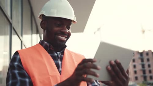 Young Handsome Smiling AfroAmerican Construction Worker in Signal Jacket and White Helmet Actively