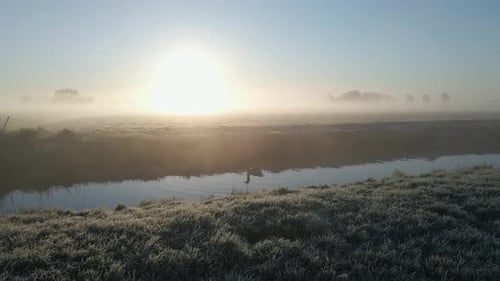 Aerial view of misty countryside at sunrise over meadow and farm, Netherlands.