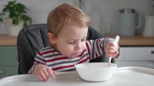 Toddler Eating Cereal with a Spoon in Kitchen