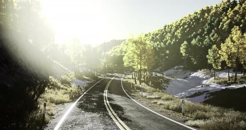 Scenic Winding Road Through Green Hills with Sunlight Shining in Background
