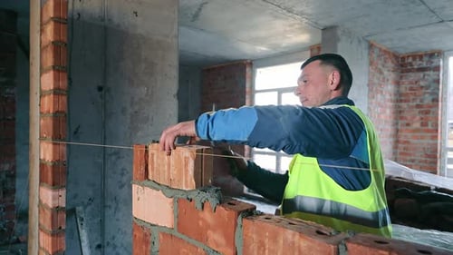 A Mason in a Vest Meticulously Building a Brick Wall Inside a Construction Site The Builder