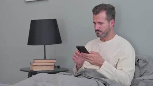 Man Using Smartphone in Bed at Home