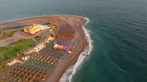 Mediterranean beach with colorful umbrellas and calm waves breaking on shore at sunrise