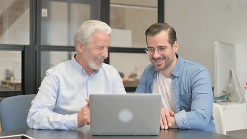Senior and Young Adult Collaborating on Laptop in Office