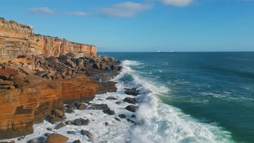 Drone view of stormy sea waves crashing on rocky seashore coastline on sunny day