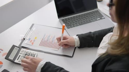 A Skilled Professional Analyzes Financial Data with a Calculator and Laptop Reviewing Reports and