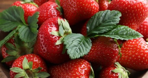 Fresh ripe strawberries in bowl spinning on table, closeup