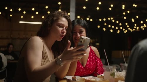 Multiethnic Female Friends Viewing Pictures In Smartphone And Laughing Dining In Restaurant
