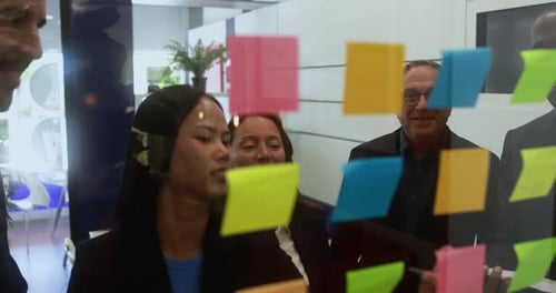 Multiracial colleagues working inside business office with glass walls and adhesive note