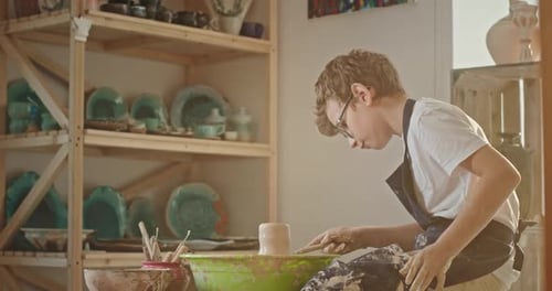 Ein junger Teenager, der mit Töpfern beschäftigt ist und auf einer Töpferscheibe sitzt, malt eine Zeichnung auf einer Töpferei