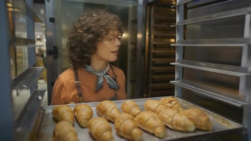Woman Removing Croissants from Cooling Rack in Bakery