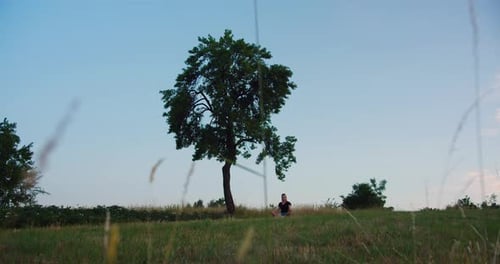 Woman practises yoga at sunrise on a meadow. Young spiritual girl meditates in lotus pose